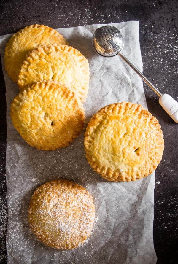 hand pies on parchment paper with one sprinkled with icing sugar