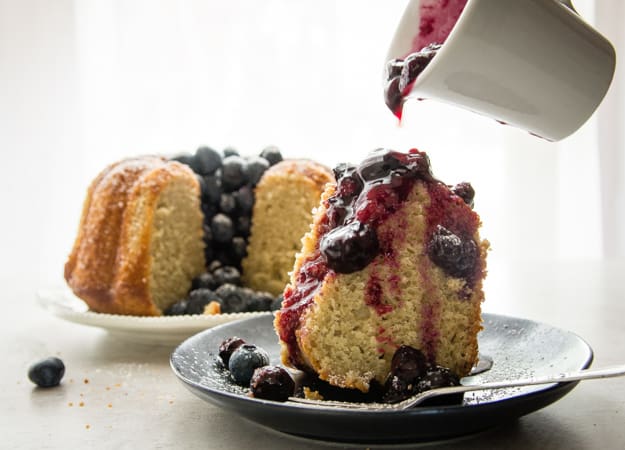 a slice of easy yogurt cake with blueberry sauce pouring from a white bottle