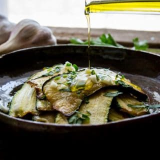 marinated zucchini in a bowl with parsley and chopped garlic, drizzling oil on top