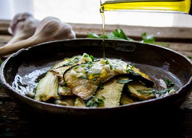 marinated zucchini in a bowl with parsley and chopped garlic, drizzling oil on top