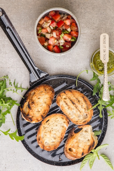 grilled bread on the grill pan with tossed tomatoes & onions in a small bowl