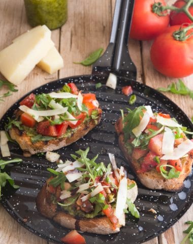 bruschetta made on a black round grill pan with tomatoes, parm and pest in the background