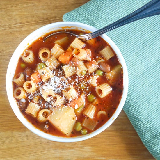 a bowl of minestrone soup with a silver spoon