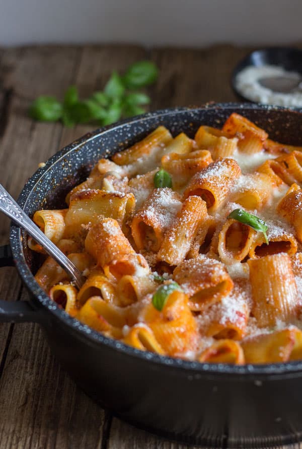 a skillet of baked pasta with a spoon in it and sprinkled with parmesan cheese