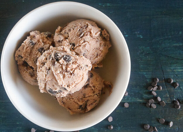 4 scoops of gelato in a white bowl on a blue board with a silver spoon and chocolate chips sprinkled