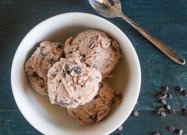 4 scoops of gelato in a white bowl on a blue board with a silver spoon and chocolate chips sprinkled