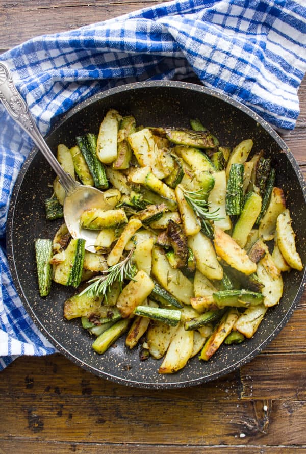 Pommes de terre courgettes rôties dans une poêle noire avec une cuillère de service argentée et une serviette bleue et blanche