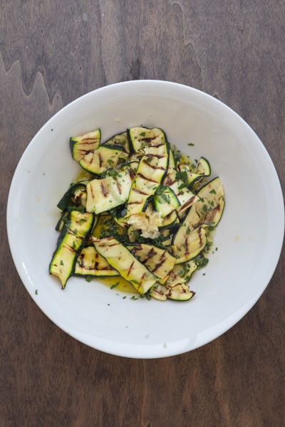 Zucchini with oil, garlic and parsley on a white plate.