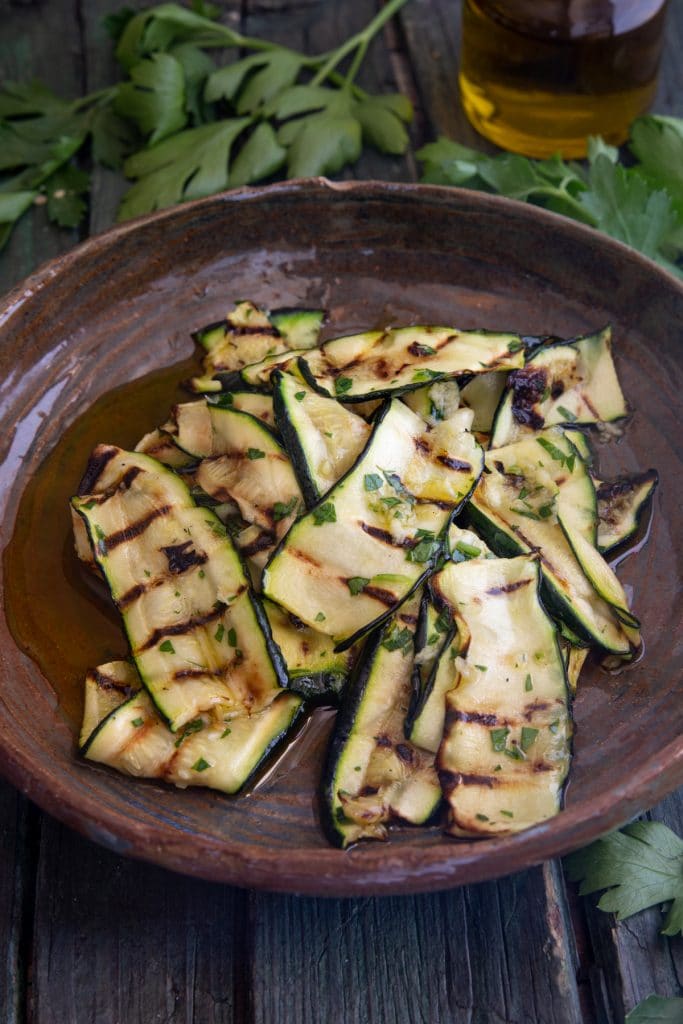 Zucchini on a brown plate with olive oil in a small jar.