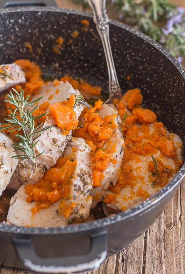 cooked roast pork loin sliced with carrots in a black pan