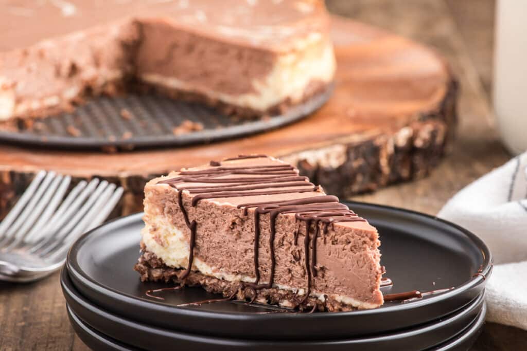 Cheesecake on a black plate with a slice drizzled in chocolate on a plate.