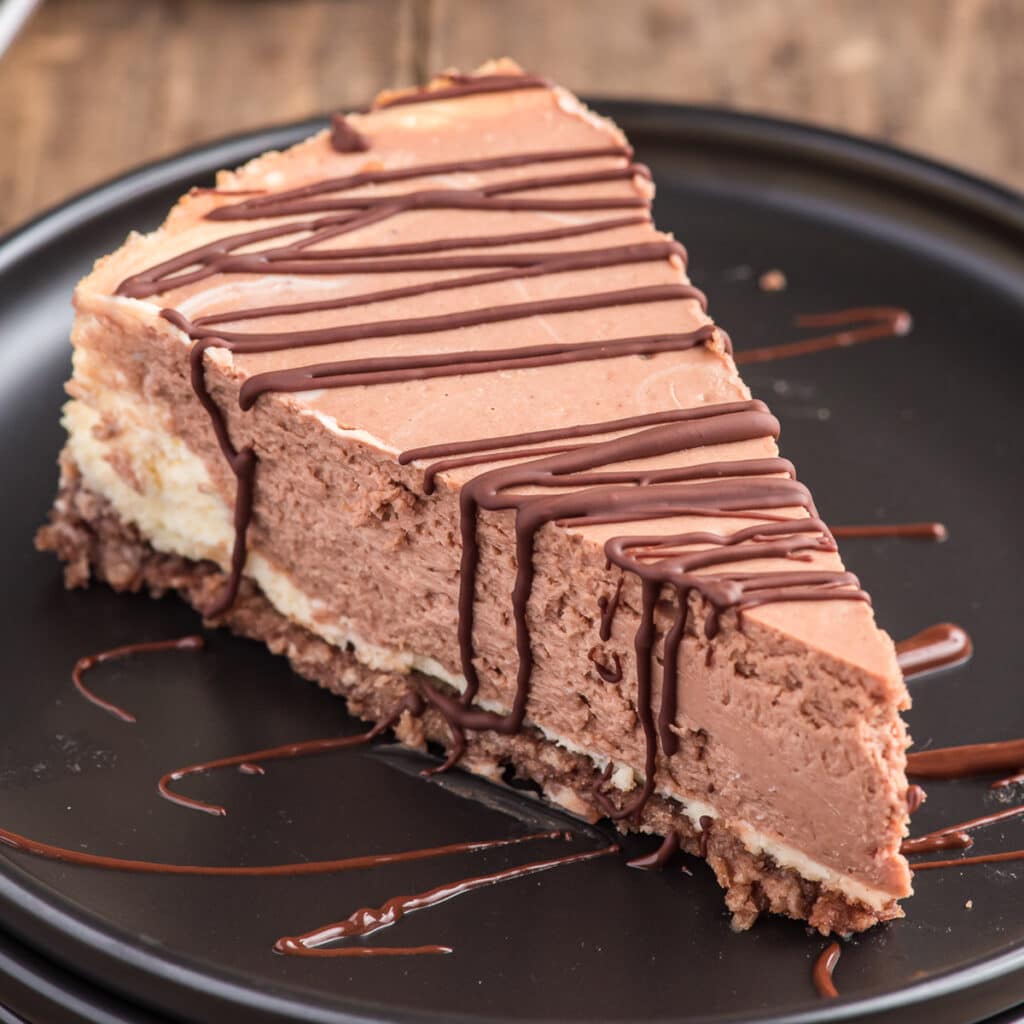 Cheesecake on a black plate with a slice drizzled in chocolate on a plate.