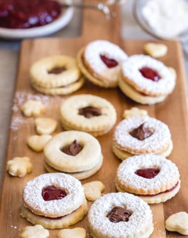Italian sandwich cookies on a board with jam and powder sugar