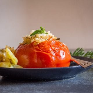 tomatoes stuffed with rice on a black plate with roasted potatoes