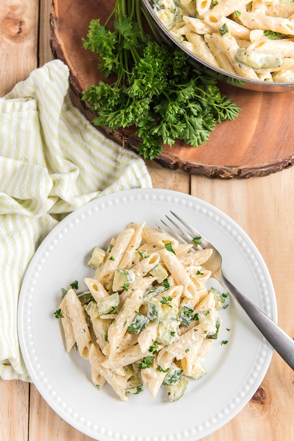 pasta on a white plate with a fork and a green napkin, parsley on a wooden board