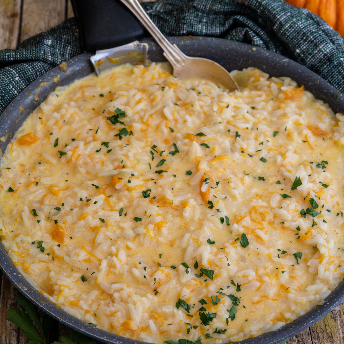 Pumpkin risotto in a black pan with a spoon.