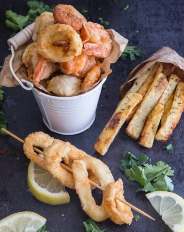 fried seafood in a small white bucket with calamari on a stick and fries in a small paper bag