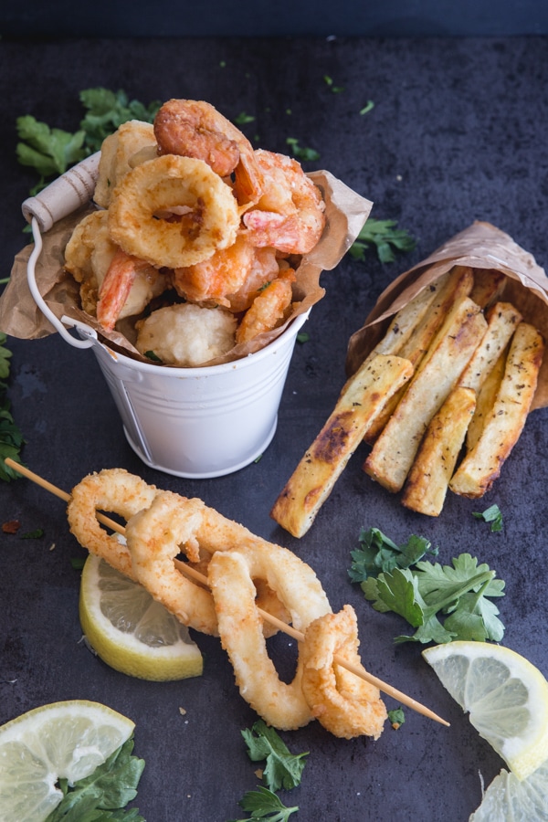 fried seafood in a small white bucket with calamari on a stick and fries in a small paper bag