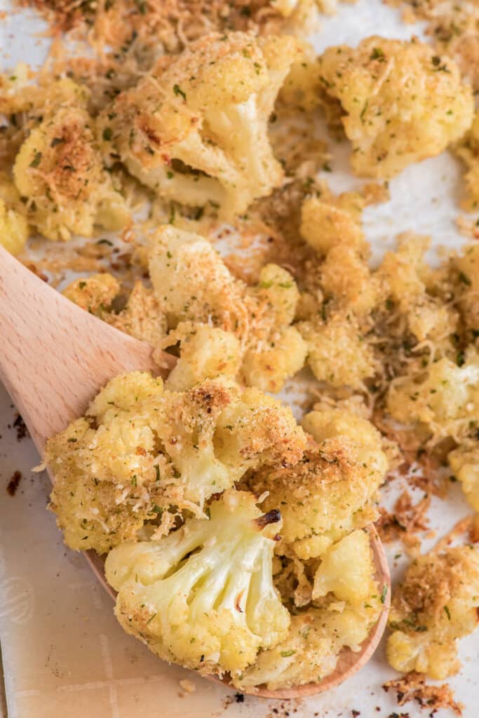 Roasted cauliflower on a pan and some on a wooden spoon.