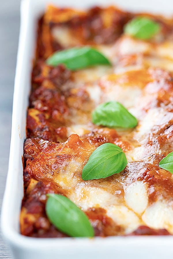 lasagna in a white pan with basil leaves on top