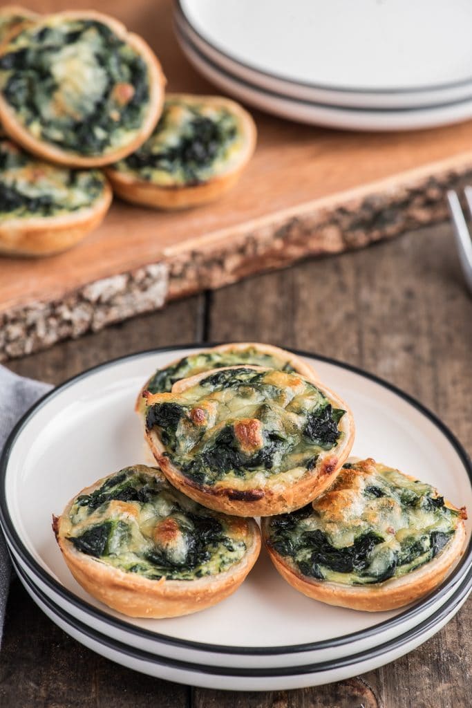 Ricotta spinach tarts on a board and 3 on a white plate.