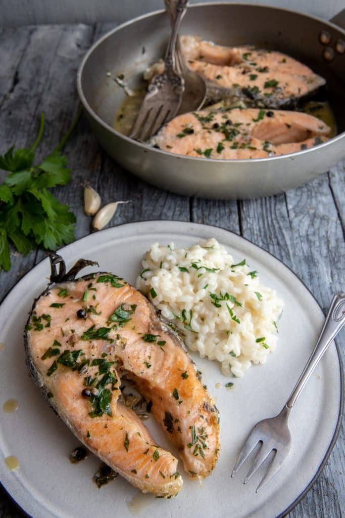 Salmon steaks in a pan and one on a plate with rice.