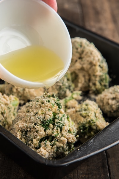 Pouring olive oil over the breaded broccoli in the baking pan before baking.