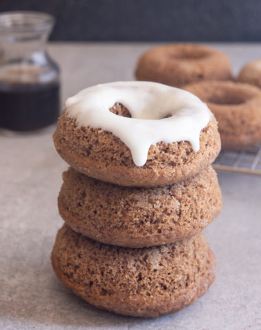 3 mocha donuts stacked with 3 on a wire rack and cream cheese frosting on top of one.