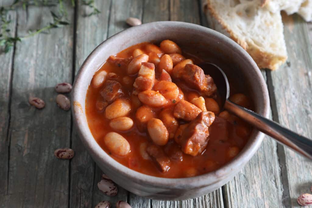 Prosciutto bean soup in a blue bowl with two slices of bread.