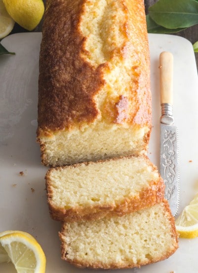 lemon bread with 2 slices, a slice of lemon and a knife on a white board