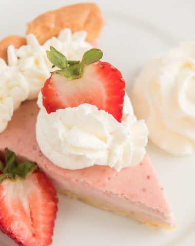 a slice of pie on a white plate with whipped cream and a slice of strawberry on top