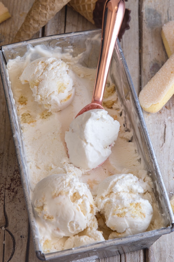tiramisu ice cream in a silver container with three scoops and a copper ice cream scoop