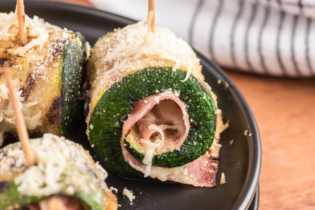 Up close a zucchini rollup on a black plate.