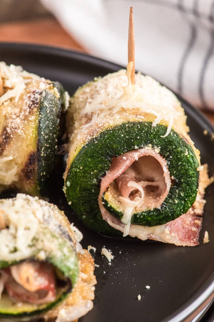 Up close a zucchini rollup on a black plate.