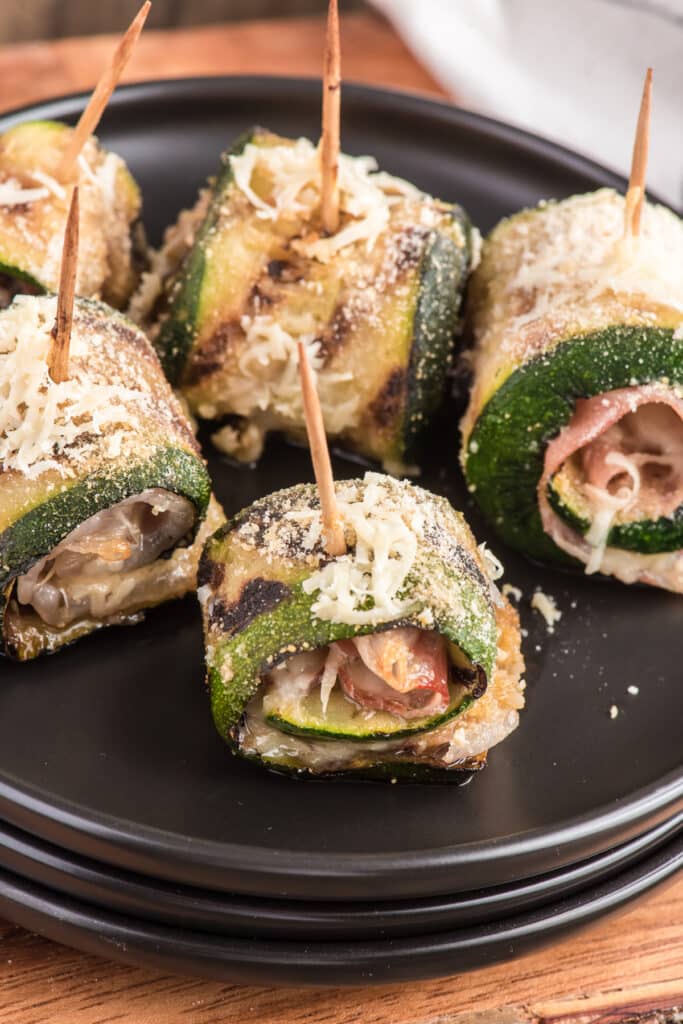 Zucchini rollups on three black plates that are stacked.