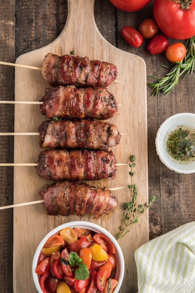 The pork & beef skewers on a wooden board with a tomato salad.