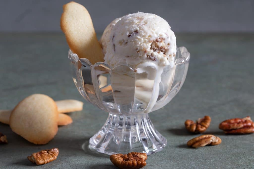 Ice cream in a glass bowl with some flat cookies.