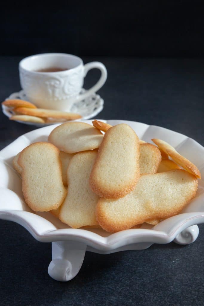 Flat cookies on a white plate with a cup of tea.