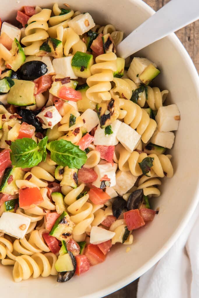 Pasta salad up close in a white bowl with a spoon.