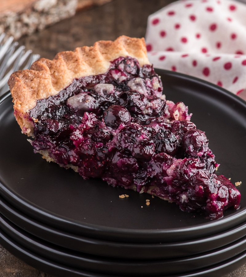 A slice of blueberry pie on a black plate.