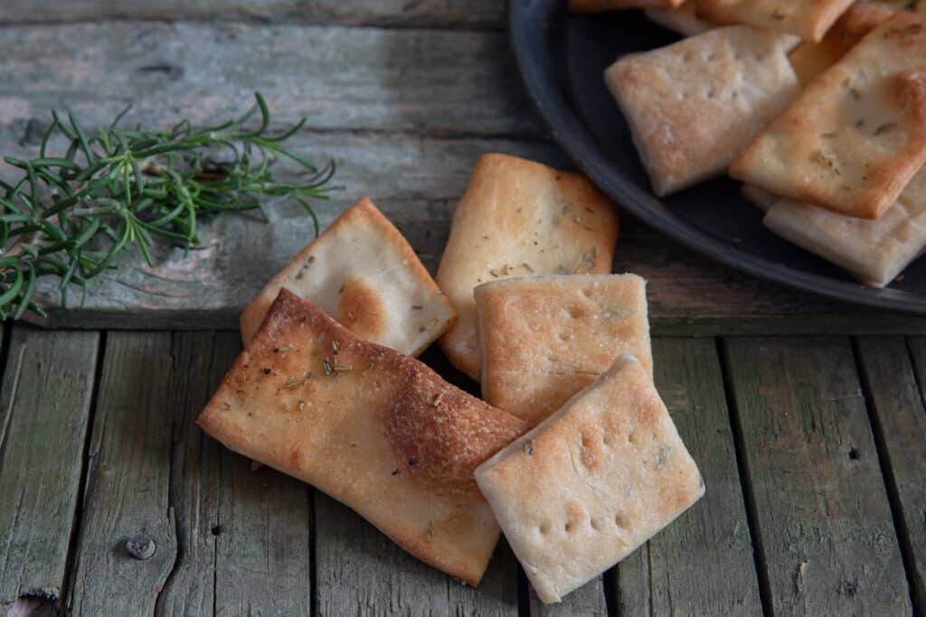 The crackers on a black plate and some on a wooden board.