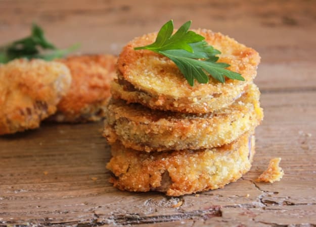 3 breaded eggplant slices one on top of the other and 2 in the background