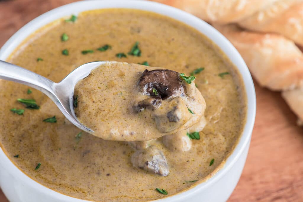 Soup in a white bowl with some on a spoon.