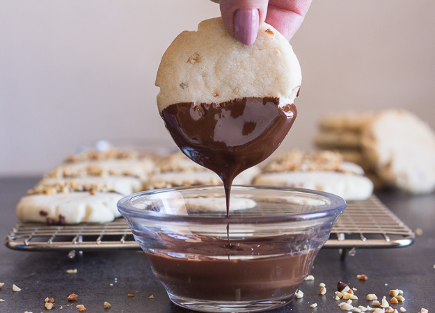 dipping a chocolate hazelnut shortbread cookie into some melted chocolate