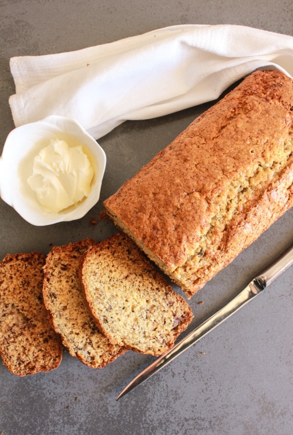banana bread with 3 slices, a knife and butter in a white dish