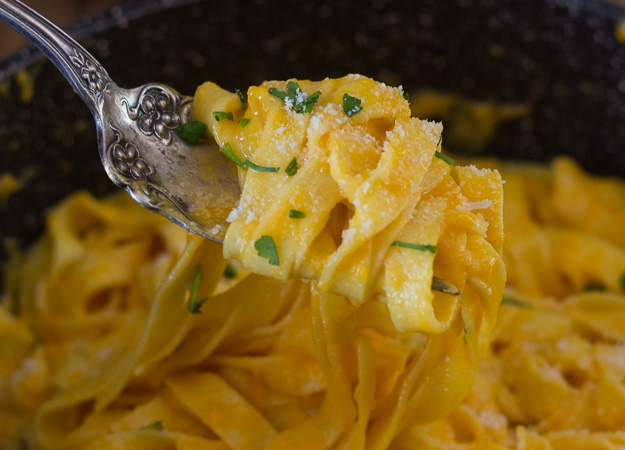 a close up of creamy pumpkin pasta sauce noodles on a fork