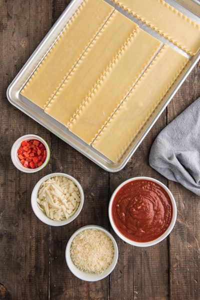 Lasagna noodles and ingredients on a wooden board.