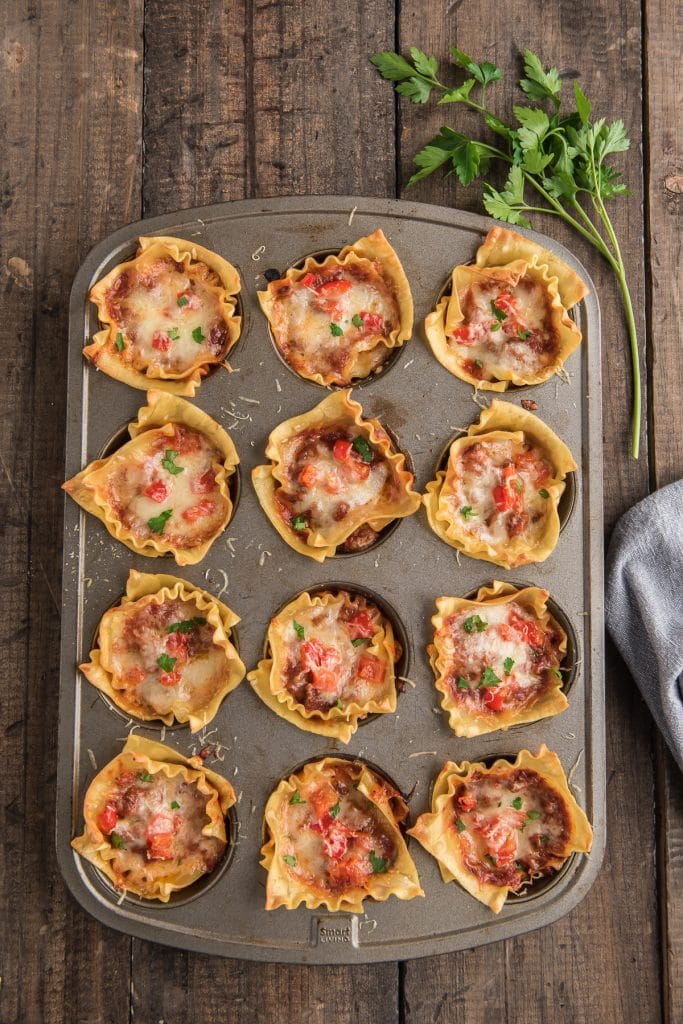 Rustic lasagna cups in a muffin tin on a board.