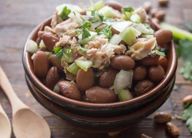 bean salad with chopped parsley on top in a brown bowl with wooden spoons