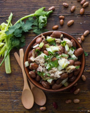 bean salad with chopped parsley on top in a brown bowl with wooden spoons